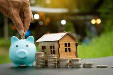 Subsidies en leningen voor energiebesparing weergegeven met spaarvarken, stapels munten en een houten huismodel.