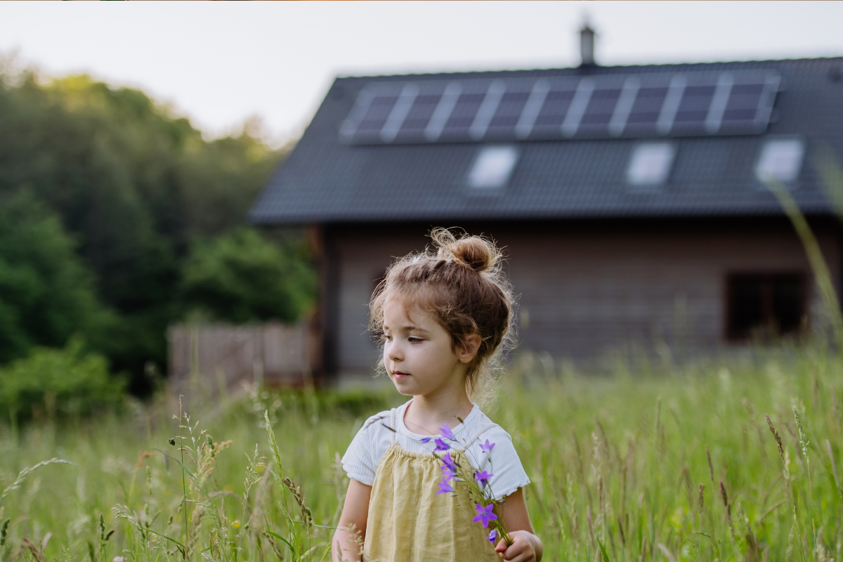 Zonnepanelen op het dak van een huis met een meisje dat in het gras een bloem vasthoudt.