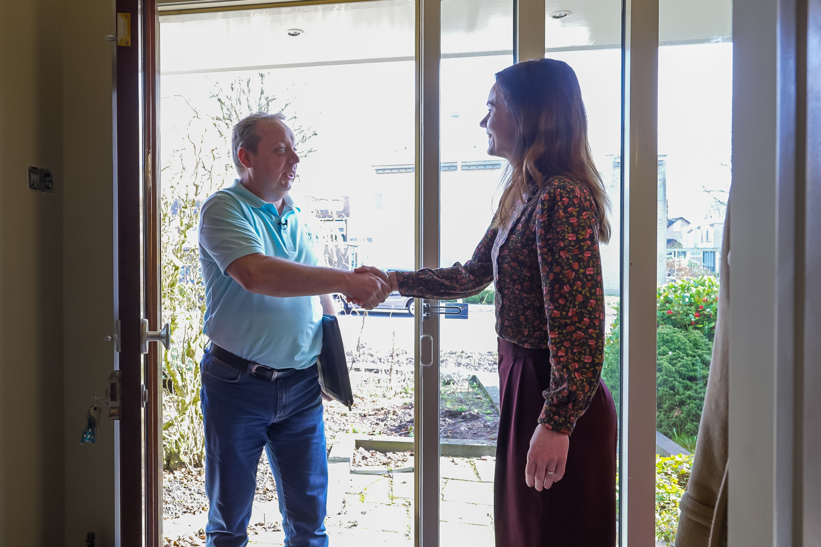 Overdracht van nieuw huis tussen twee personen bij de voordeur, start van duurzaam wonen.